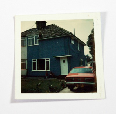 Polaroid photo of blue semi-detached house with red car