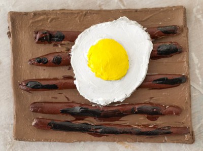 A dish of sausages and a fried egg made out of clay